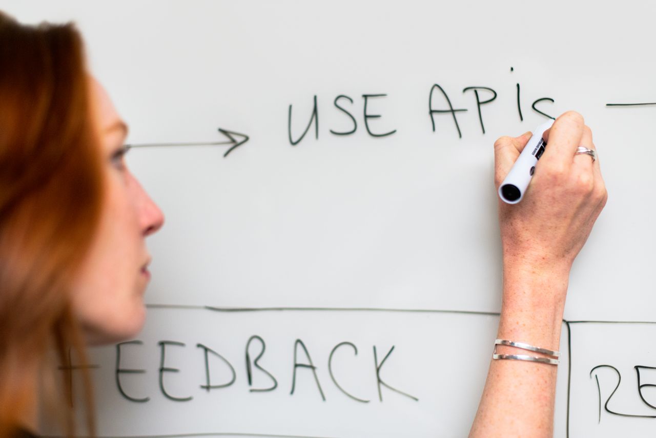 services-03 A woman writes Use APIs on a whiteboard, focusing on software planning and strategy.